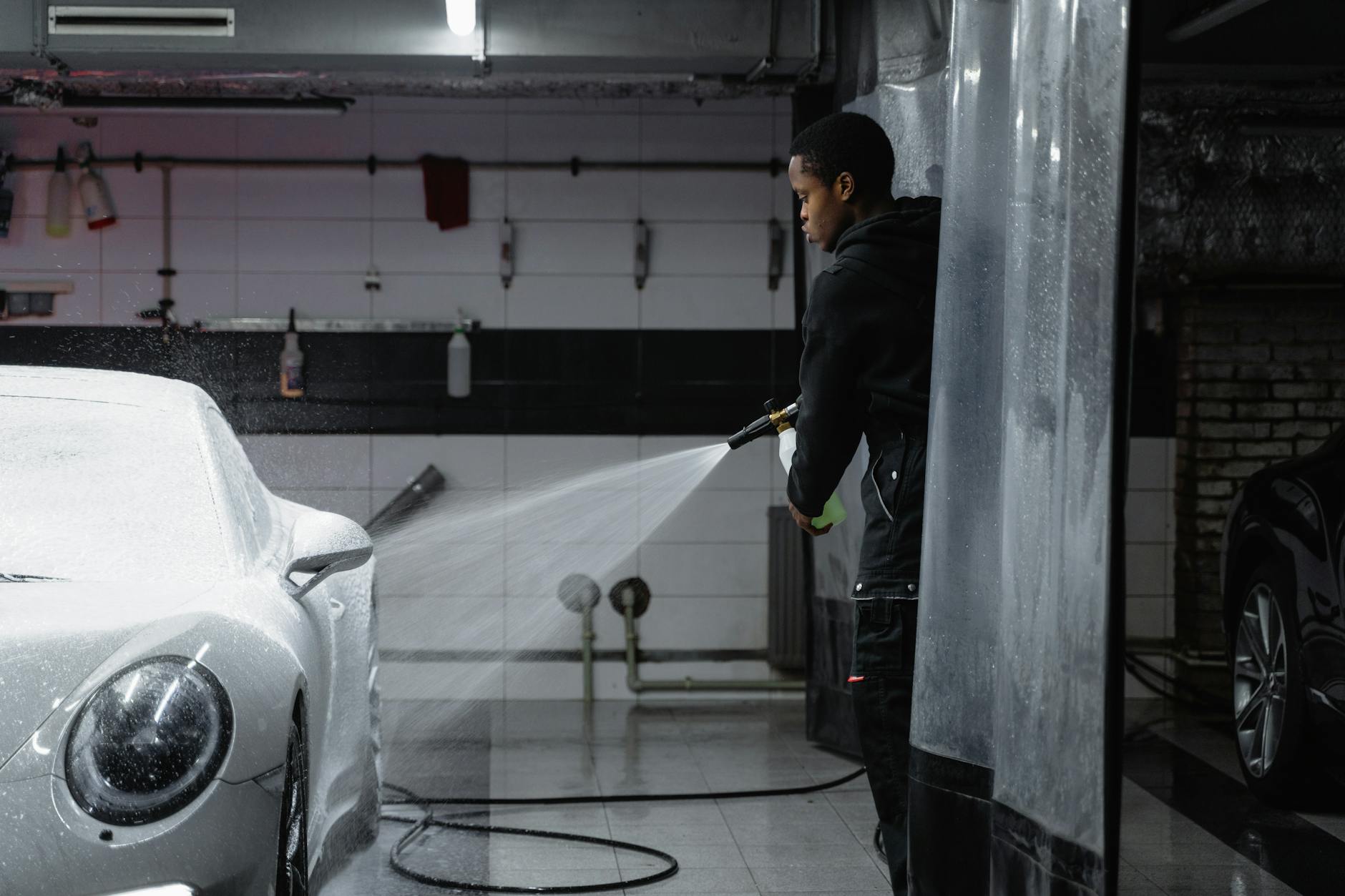 A person using a pressure washer to clean a car in an indoor garage setting.