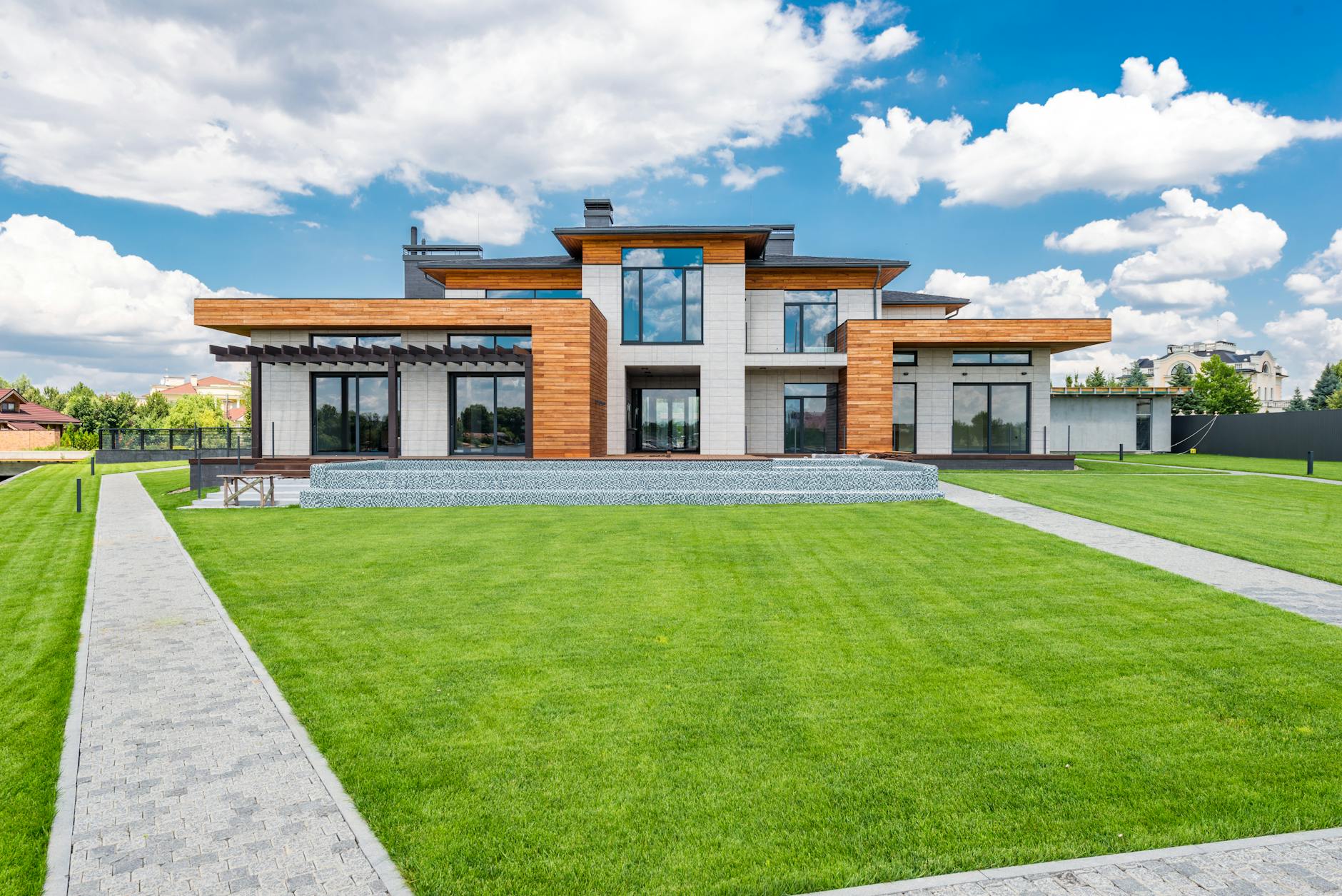 Exterior of contemporary residential house with glass doors and panoramic windows near green lawn with paved paths on sunny day in summer